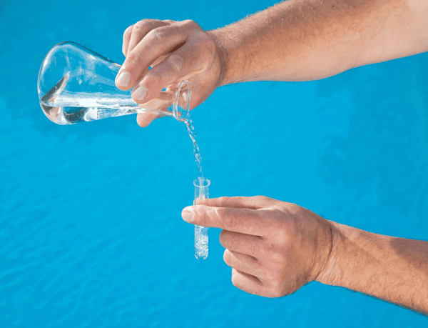 Hands pouring water from flask into test tube.