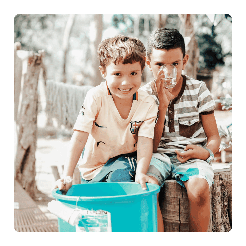 Two boys sitting by a blue bucket.
