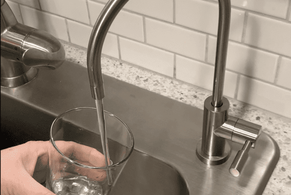 Hand filling glass under kitchen faucet.